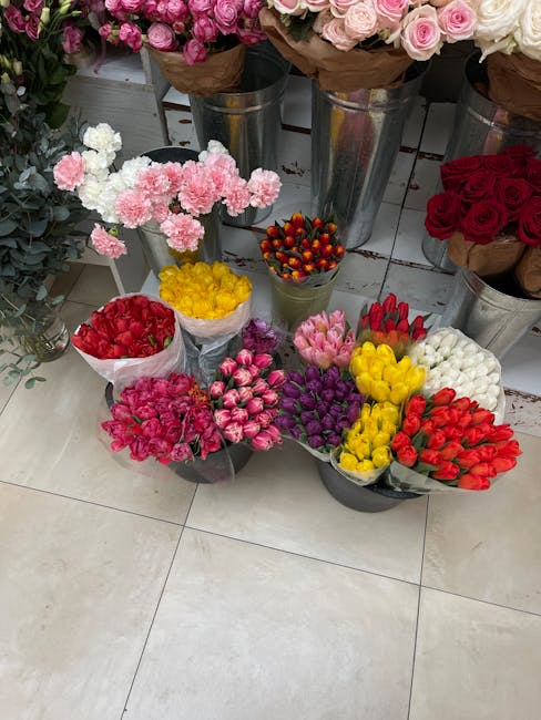 A selection of fresh flower bouquets and individual stems arranged on a tiled floor in a flower shop. The display includes pink, red, yellow, purple, and white blooms, with some wrapped in paper and o