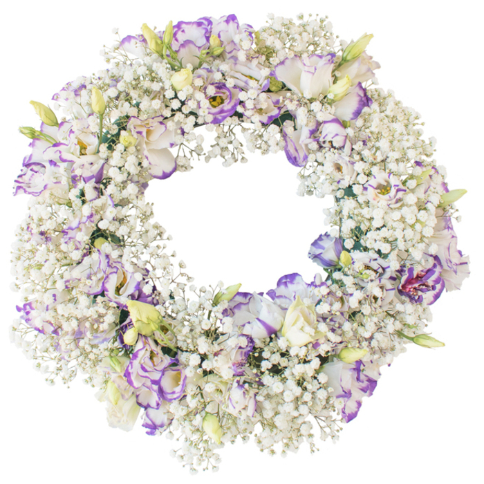 A delicately crafted funeral wreath fills the frame, presented against a pure white background that highlights every nuance of its flowers. The wreath forms a flawless circle, its structure completely hidden beneath a thick garland of white Baby's Breath that resembles a ring of soft foam or early mist settling over Norbury's quiet back gardens. Each slender stem of Gypsophila is heavily dotted with tiny, star-like blossoms, lending a feather-light but visually dense texture that feels both comforting and serene. Interlaced among this snowy expanse are numerous Lisianthus blooms, poised like gentle accents around the circle. Their petals are fine and slightly ruffled, layered to create a sense of depth and movement. The main tone is crisp white, while the outer edges and delicate veins are kissed with cool shades of lavender and deeper purple-violet, giving each flower a painterly border that stands out against the luminous Baby's Breath. Some Lisianthus are shown fully opened, revealing softly shadowed interiors; others are partially closed or in tight bud, introducing hints of pale green and creamy yellow that suggest fresh growth and continuity. The centre of the wreath is left open and unobstructed, reinforcing its classic symbolism of eternity, unity, and everlasting love. It is easy to imagine this design resting at a funeral service in Norbury or laid at a graveside in a local cemetery as a quiet, refined message of remembrance. With no additional adornment, the composition remains focused on pure form and gentle colour, conveying a mood of dignified sympathy and tender respect.
